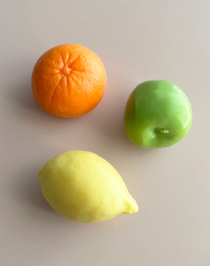 Orange, lemon, and green apple fruit shaped soaps on a light grey background